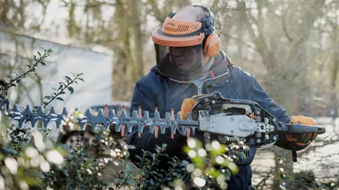  Ein Mitarbeiter im Bereich Garten- und Landschaftsbau schneidet eine Hecke